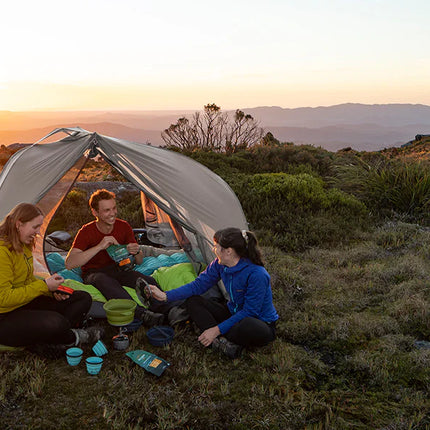 Friends camping outdoors with gear and a tent set up in a scenic natural setting, surrounded by beautiful landscape scenery in the background.