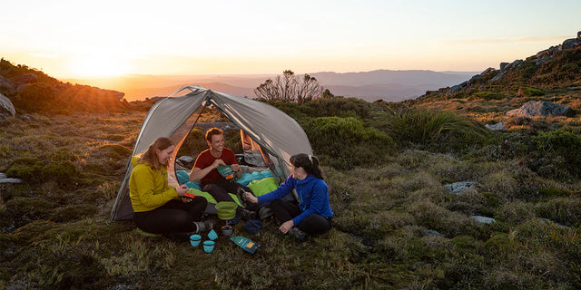 Friends camping outdoors with gear and a tent set up in a scenic natural setting, surrounded by beautiful landscape scenery in the background.