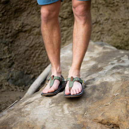 Man wearing Lems Switchback sandals while hiking on a rocky trail, stepping on a large rock with secure straps and rugged outsole visible in an outdoor setting.