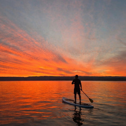 Person on stand-up-paddle board with an incredible beautiful orange sunset in the background on a smooth lake.