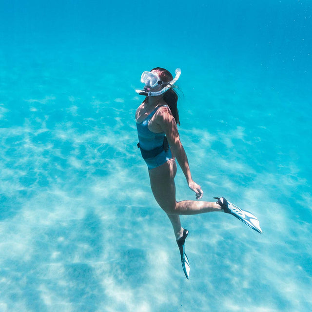 Female swimmer exploring beneath the surface in crystal clear blue water while using Seavenger snorkeling mask and fins, enjoying smooth and effortless underwater movement