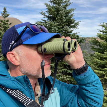Man using green Nocs binoculars with neck strap out in the forest.