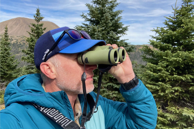 Man using green Nocs binoculars with neck strap out in the forest.
