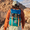 Man hiking in desert background with Topo Design Rover Pack backpack in blue, grey, adn green with orange straps.