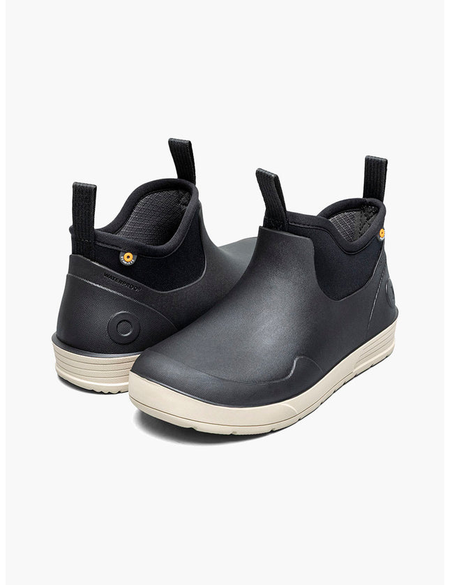 Pair of black rubber boots with white soles on a light gray background
