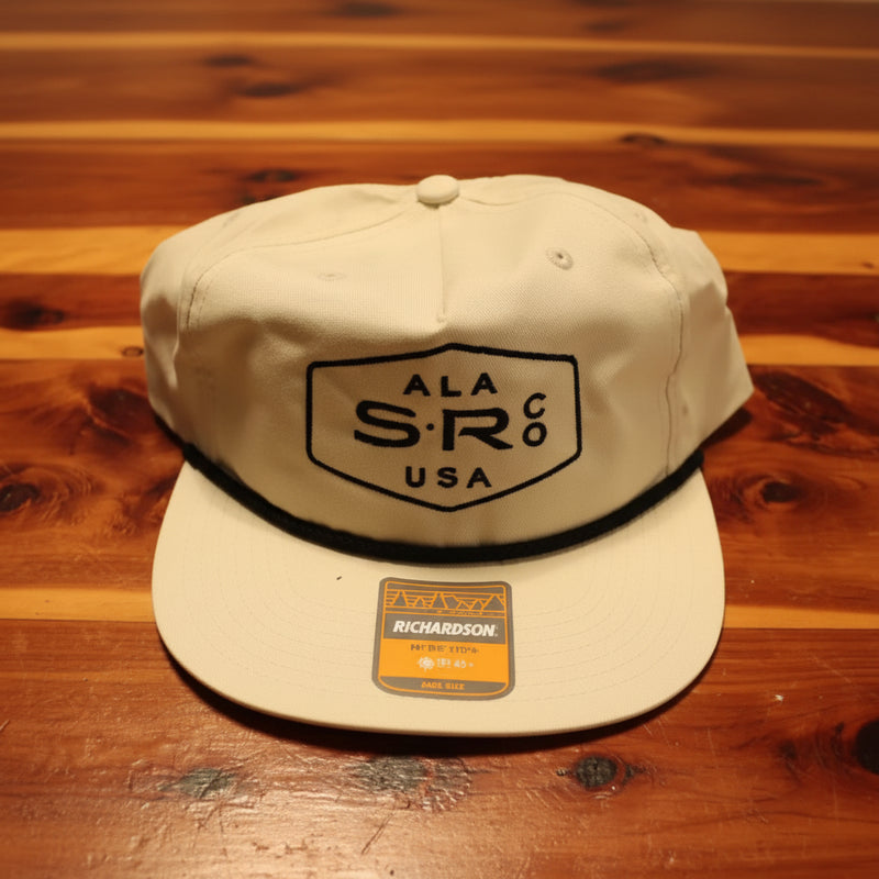 A cream-colored snapback cap with a black embroidered shield logo for Stealth Rod Co.