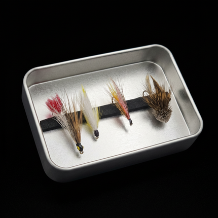 Four fly fishing flies on a metal tray against a black background