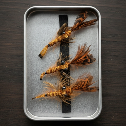 Three feathered crayfish fishing flies in a metal case on a dark background