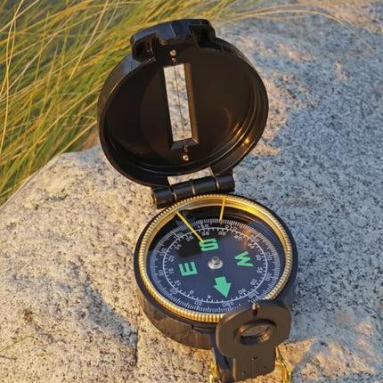 Open black and gold compass on a rock with tall grass in the background