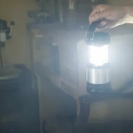 Hand holding a bright LED lantern in a dimly lit room with machinery