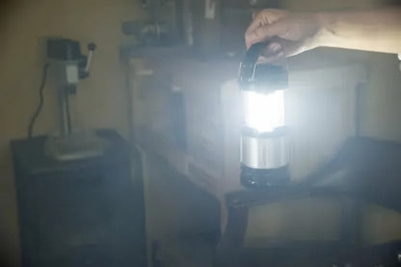 Hand holding a bright LED lantern in a dimly lit room with machinery