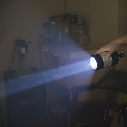 Hand holding a flashlight with a bright beam in a dimly lit room