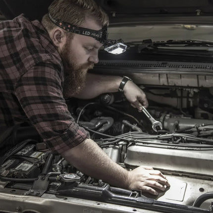 Mechanic wearing a headlamp and plaid shirt working on a car engine with a wrench
