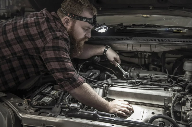 Mechanic wearing a headlamp and plaid shirt working on a car engine with a wrench