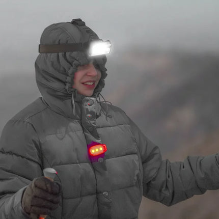 Person in a grey winter coat and headlamp, holding ski poles