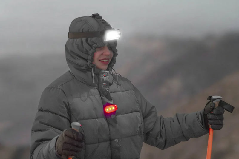 Person in a grey winter coat and headlamp, holding ski poles
