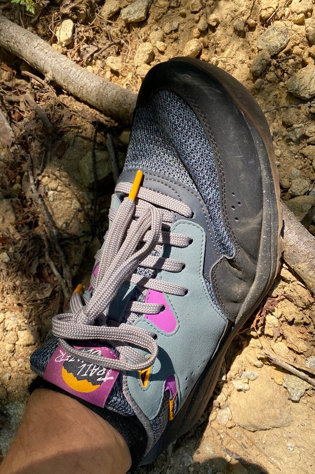 Close up of a foot wearing a grey, purple, and black trail running shoe on a dirt path