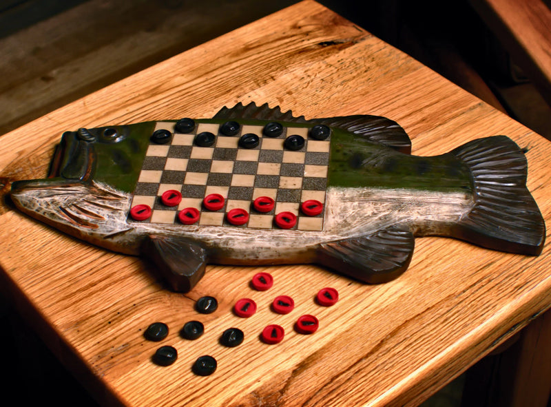 Wooden fish-shaped checkers board with checkers on a wooden surface