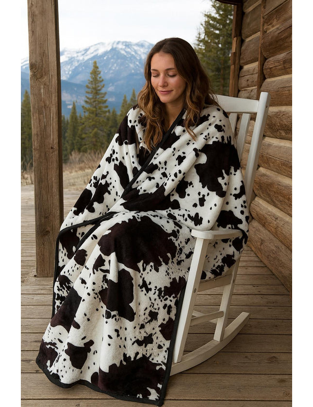 Woman sitting on a rocking chair wearing a black and white patterned blanket with a mountainous landscape in the background.