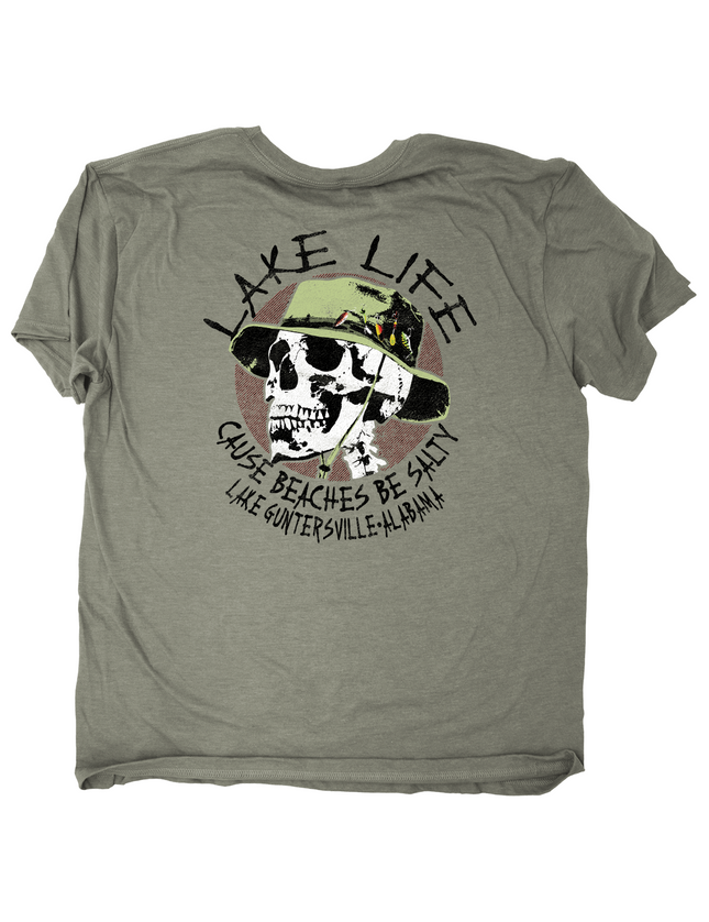 An olive green short-sleeve t-shirt with a graphic print on the front. The graphic features a skull wearing a green hat, surrounded by the text 'LAKE LIFE CAUSE BEACHES BE SALTY' and 'LAKE GUNTERSVILLE, ALABAMA'.
