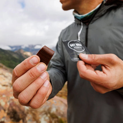 Person holding a waterless dry brew bite and its packaging with a mountainous landscape in the background