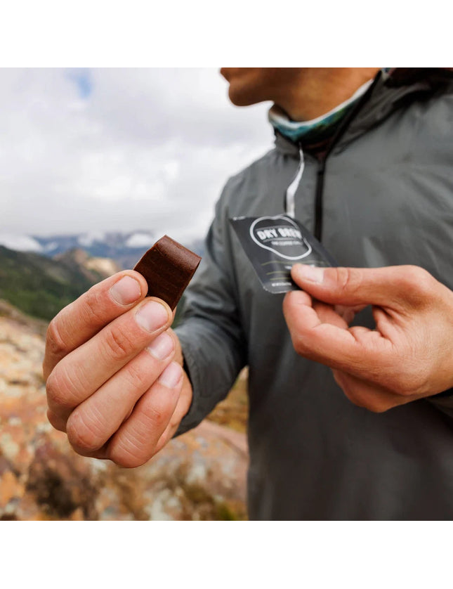 Person holding a waterless Dry Brew coffee bite and its packaging with a mountainous landscape in the background