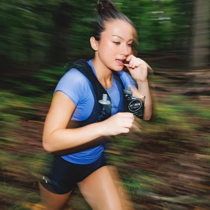 Woman running outdoors eating a dry brew coffee bite on the go.