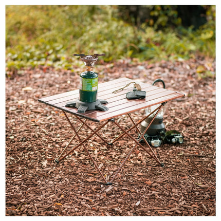 Small wooden camping table with a portable stove and other items on a natural outdoor background