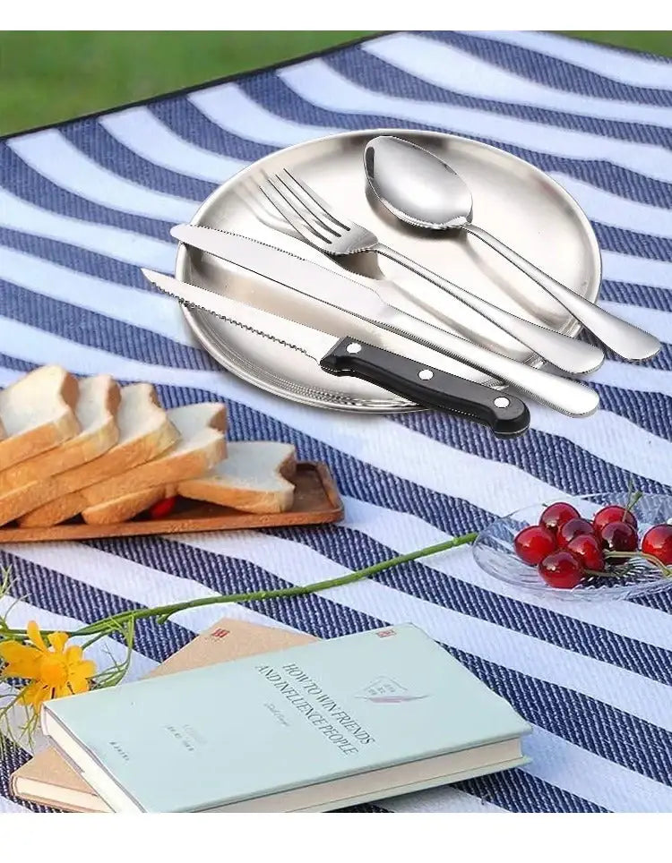 Stainless steel cutlery set on a striped blanket with bread, cherries, and a book