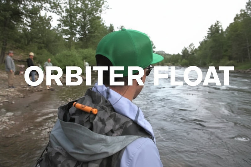 Man in green cap and grey jacket with orange item on back, looking at river with text Orbiter Float