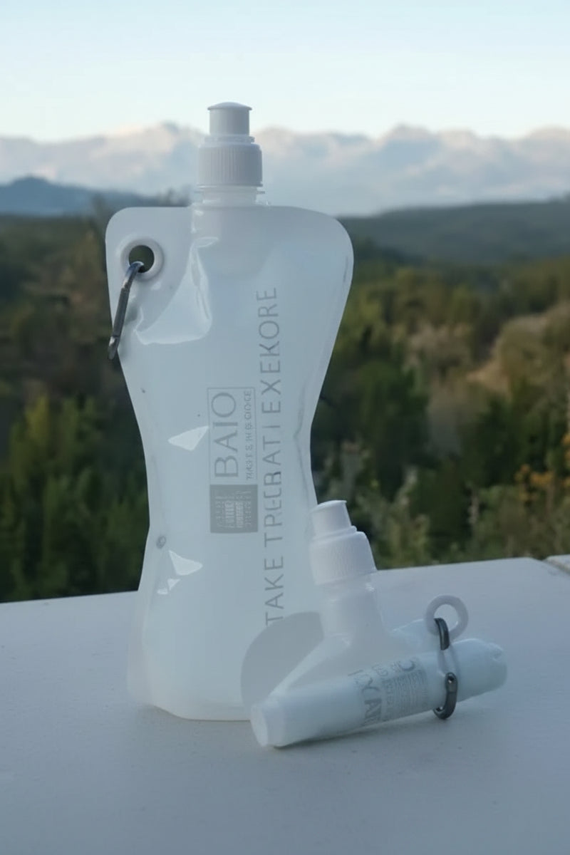 Two collapsible water bottles, one standing and one rolled, with a mountain landscape in the background