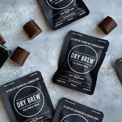 Dry Brew coffee sachets and chocolate pieces scattered on a grey surface
