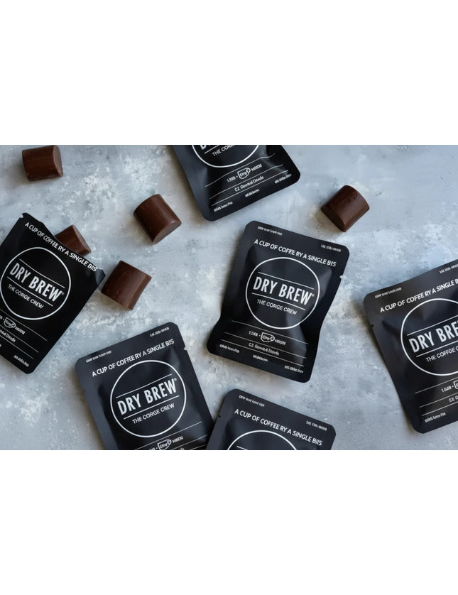 Dry Brew coffee sachets and chocolate pieces scattered on a grey surface