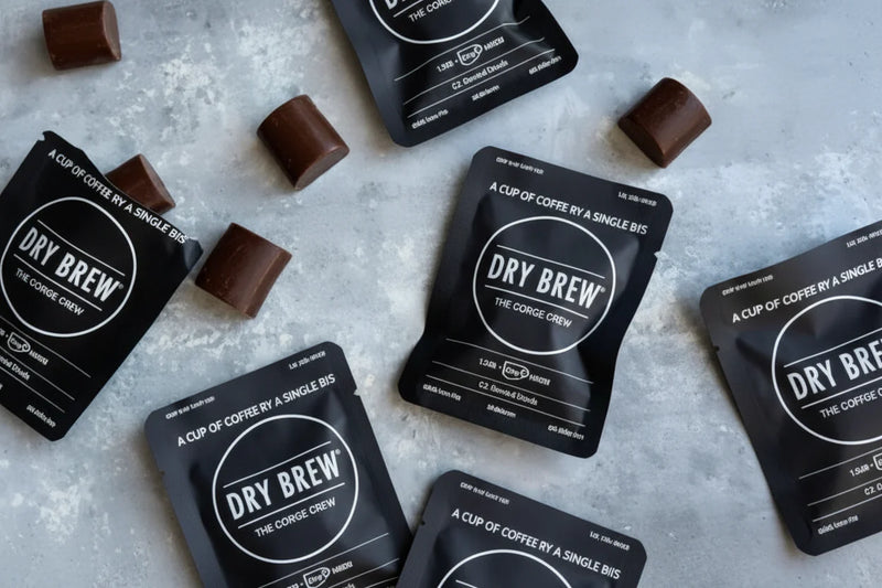Dry Brew coffee sachets and chocolate pieces scattered on a grey surface