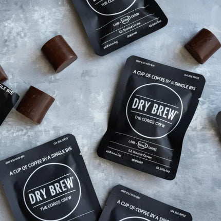 Dry Brew coffee sachets and chocolate pieces on a grey surface