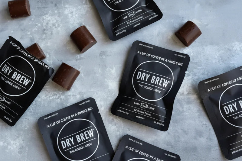 Dry Brew coffee sachets and chocolate pieces on a grey surface