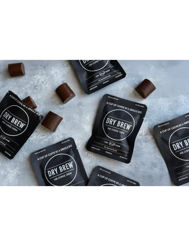 Dry Brew coffee sachets and chocolate squares scattered on a light grey surface