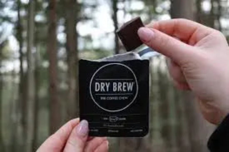 Hand holding a Dry Brew coffee chew packet, another hand placing a chocolate square into the packet