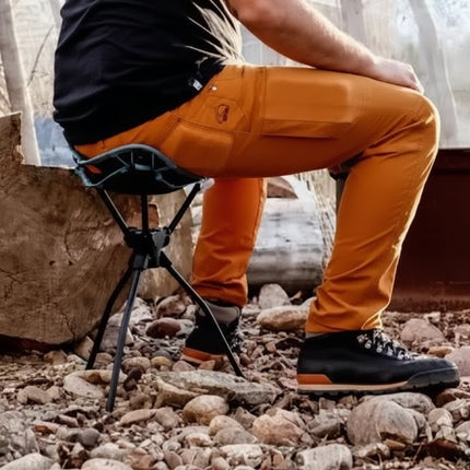Person in orange pants and black shoes sitting on a portable tripod swivel stool outdoors