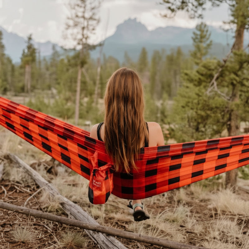 Woman with long brown hair sitting in a red and black plaid hammock in a forest