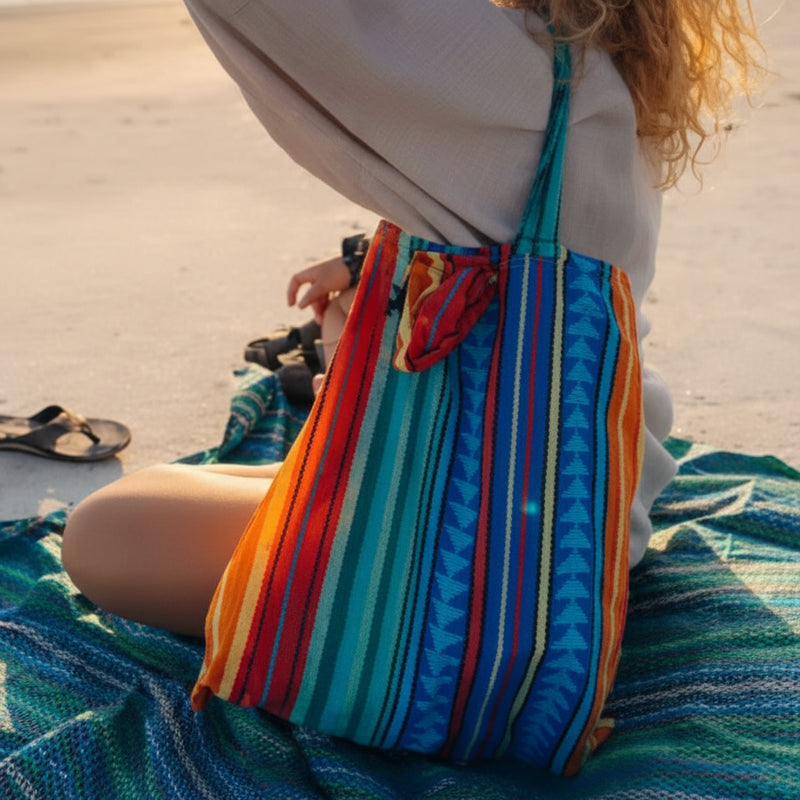 Woman sitting on a beach blanket with a colorful striped tote bag