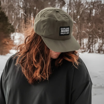 Person wearing a green cap with 'Keep It Nature Wild' logo in a snowy landscape