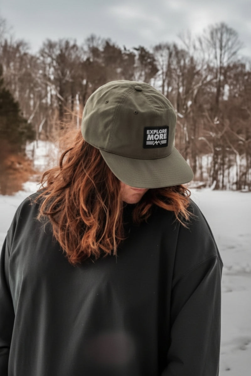 Person wearing a green cap with 'Keep It Nature Wild' logo in a snowy landscape