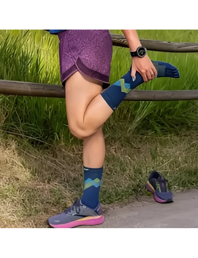 Woman stretching leg, wearing purple shorts, blue socks with green and blue pattern, and grey and pink shoes