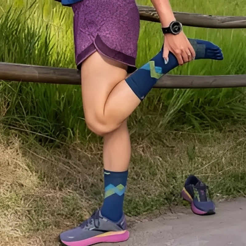 Woman stretching leg, wearing purple shorts, blue socks with green and blue pattern, and grey and pink shoes