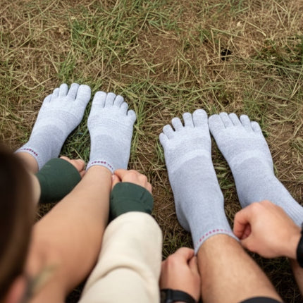 Two pairs of feet wearing grey toe socks on grass