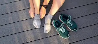 Person putting on grey toe socks, with a pair of green athletic shoes on a wooden deck