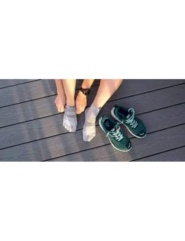 Person putting on grey toe socks, with a pair of green athletic shoes on a wooden deck