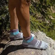 Person standing on a rock wearing grey, blue, and purple toe socks