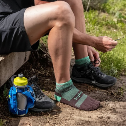 Person wearing green and brown toe socks and black trail running shoes, tying laces